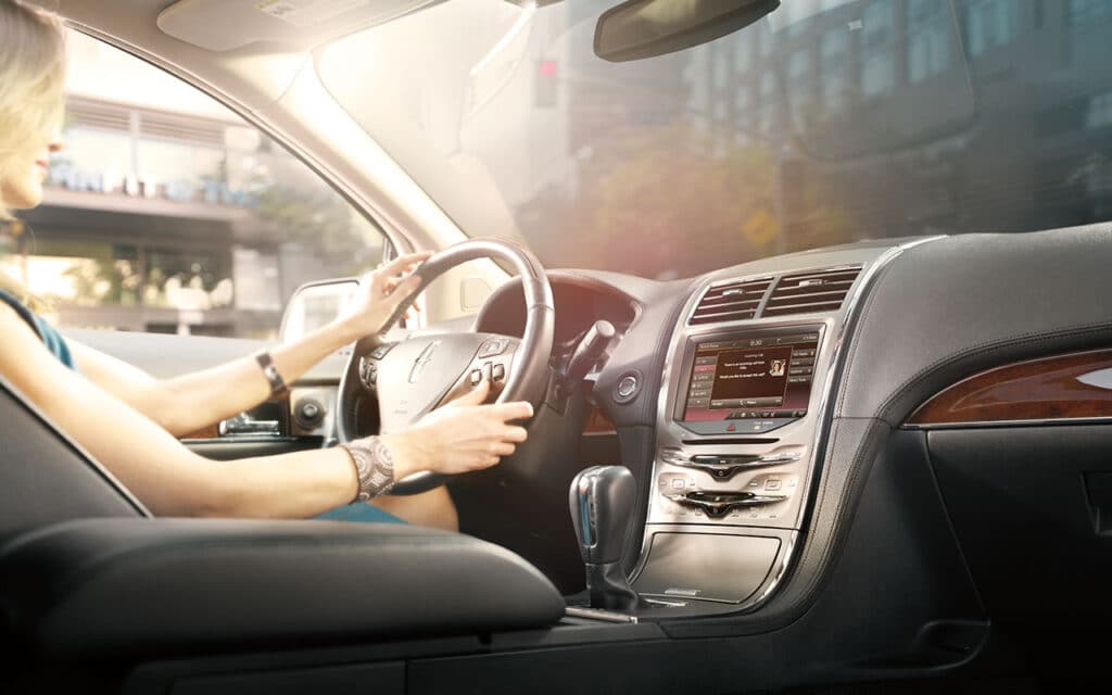 Woman driving luxury car with touchscreen dashboard, showcasing modern vehicle technology.