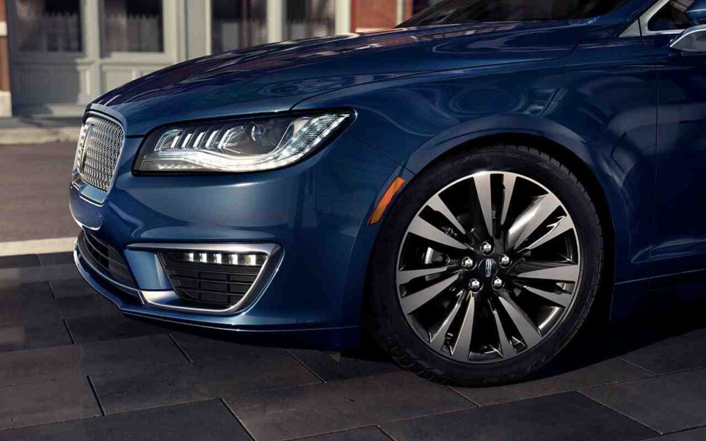 Close-up of a blue luxury car's front with sleek wheels and LED headlights, parked on a city street.