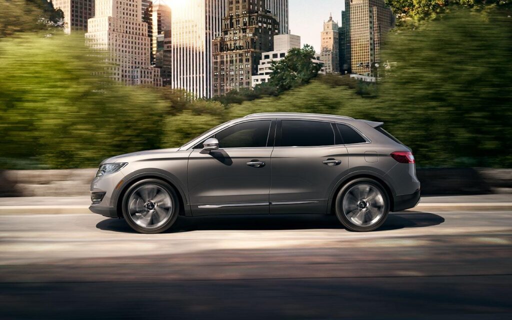 Sleek gray SUV driving through a cityscape with lush greenery and tall buildings.