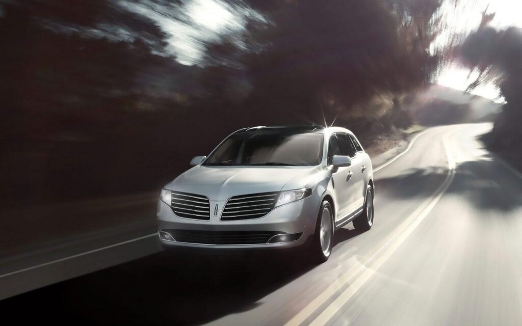 Silver luxury SUV driving on a winding road, showcasing modern design and speed.