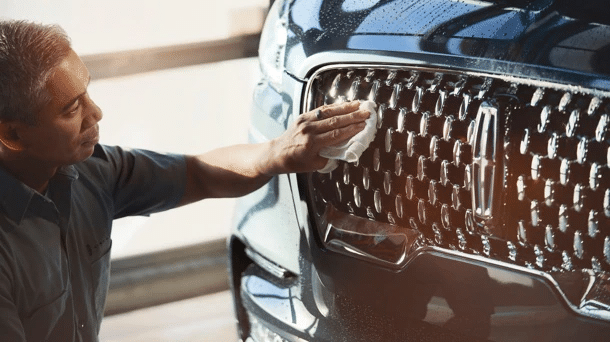 Man polishing luxury car grille with cloth for a shiny finish, emphasizing auto detailing care.