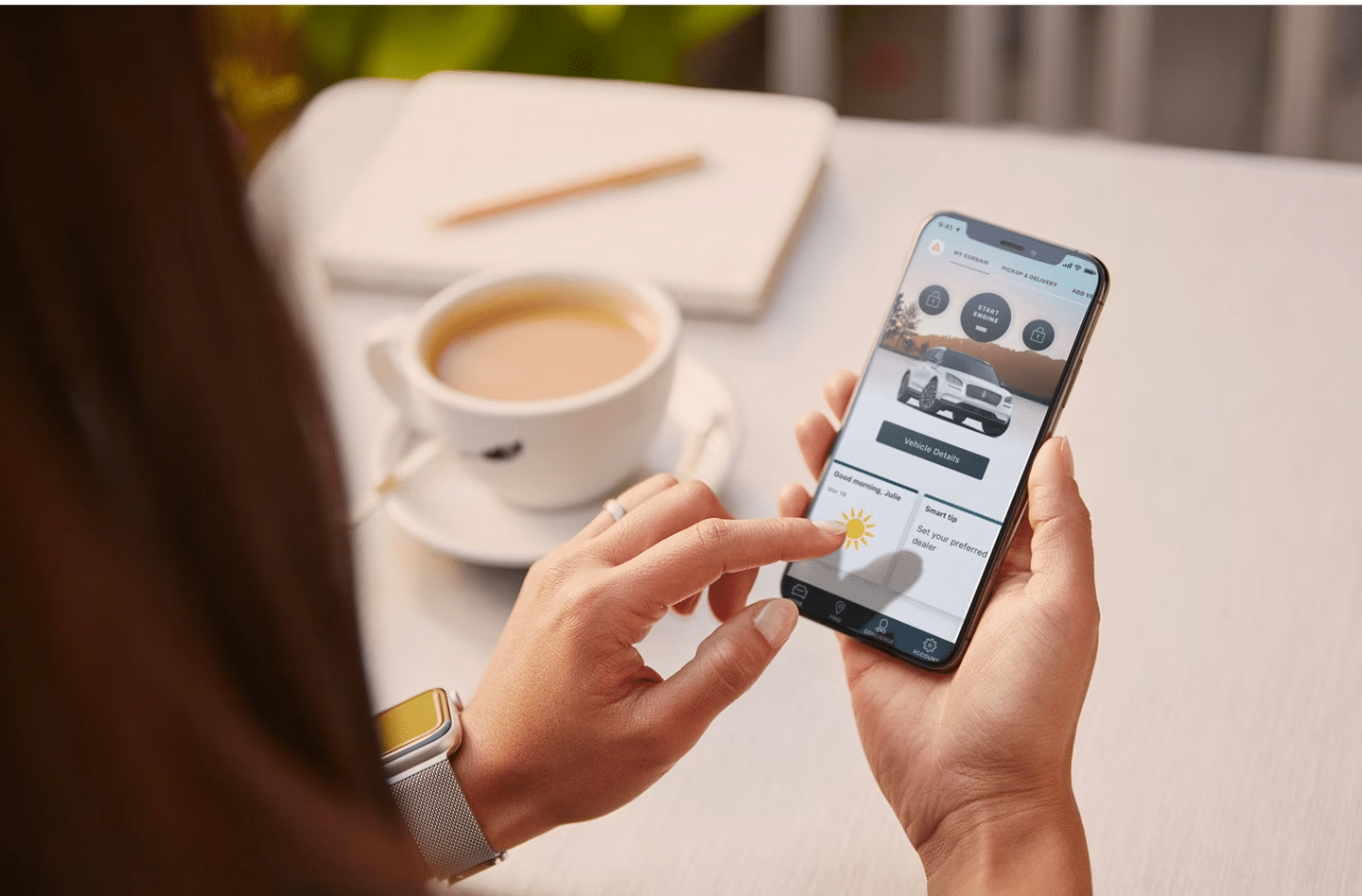 Person uses a smartphone app to check vehicle details, with a coffee cup on the table nearby.
