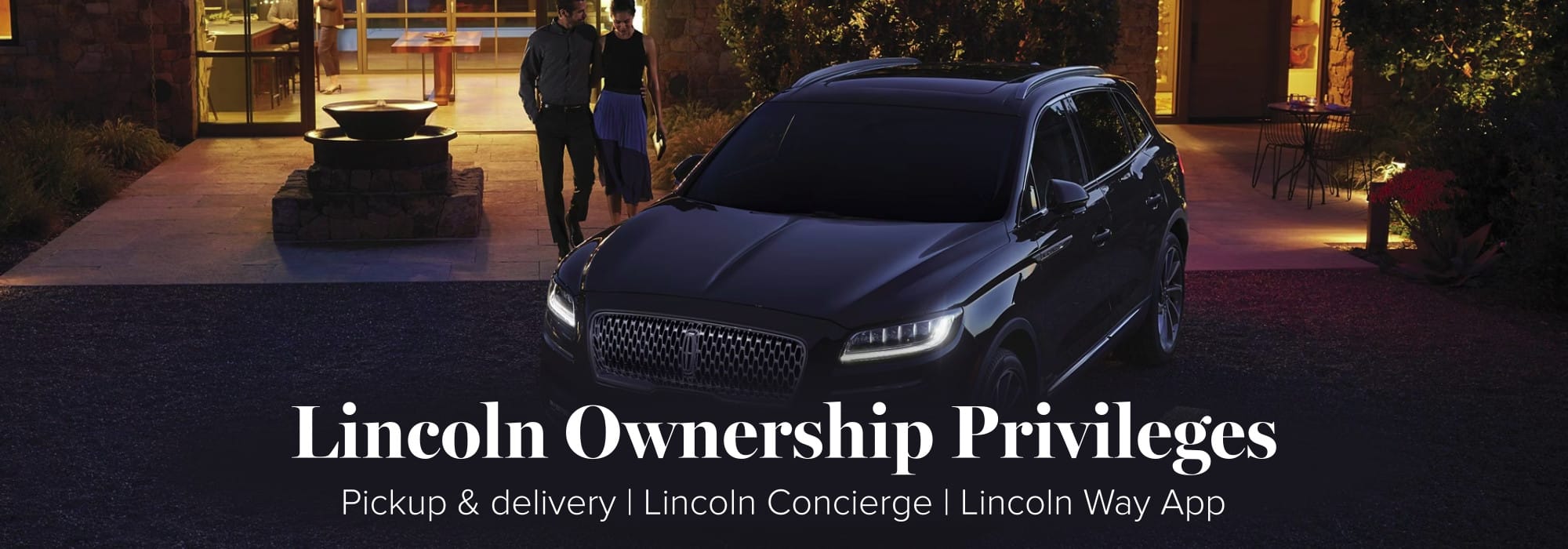 Lincolin SUV at night with a couple by modern home. Highlights Lincoln Ownership Privileges.