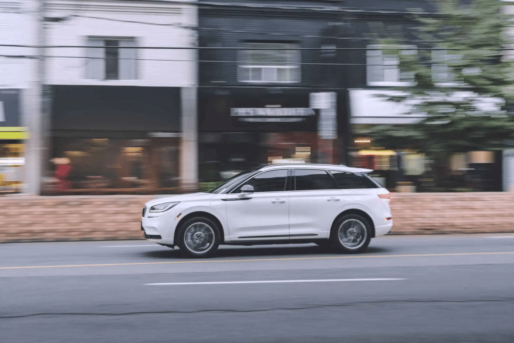 A sleek white SUV driving past urban storefronts on a city street, showcasing modern design and dynamic movement.