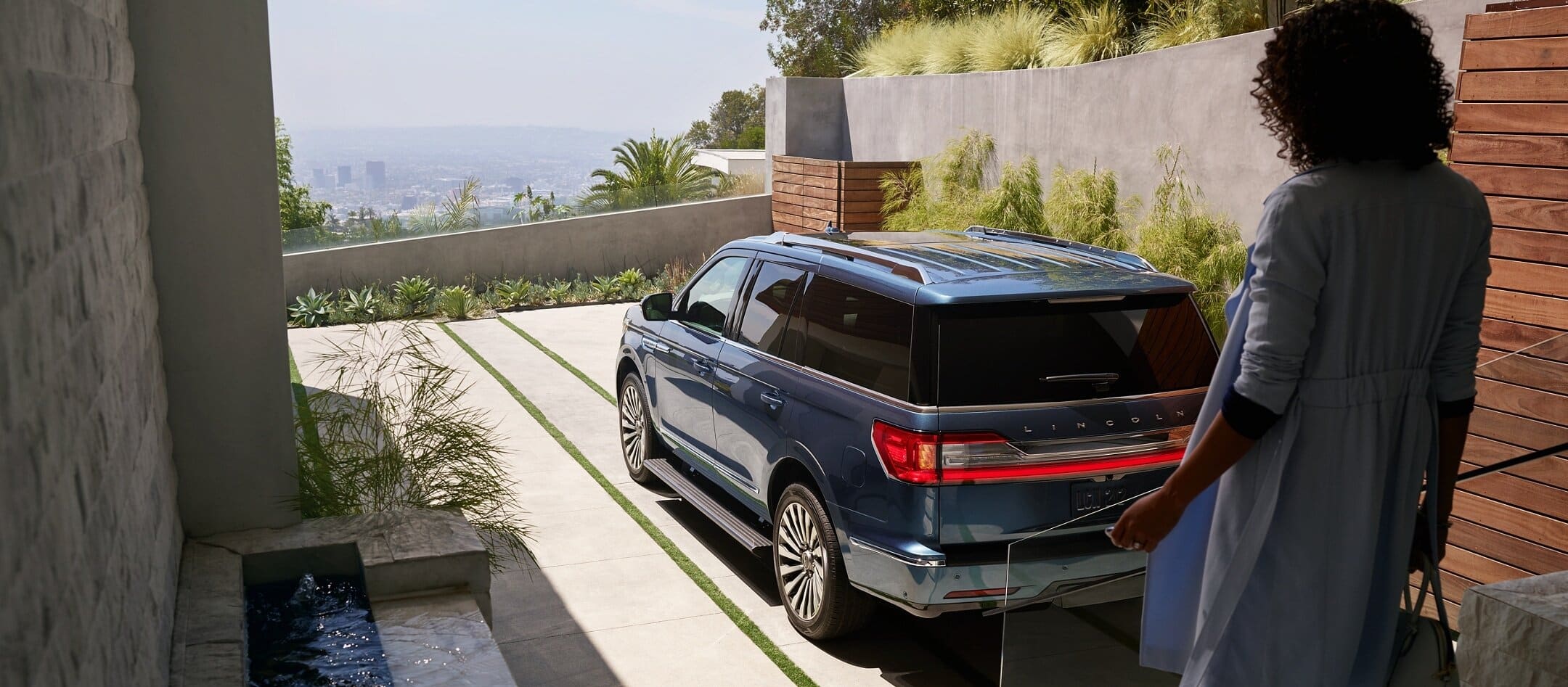 Luxury SUV parked in modern driveway with scenic view, person approaching.