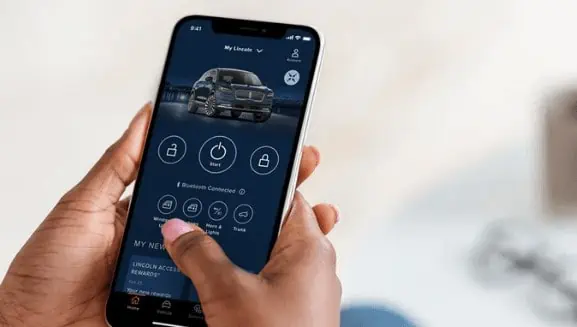 Person using a smartphone app to control car features, with icons for start, lock, and more on screen.
