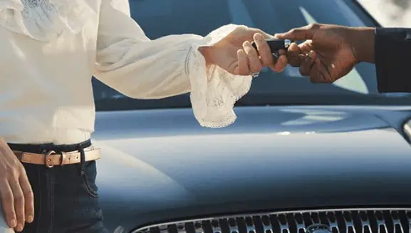Person handing over car keys in front of a luxury vehicle, symbolizing new car ownership.