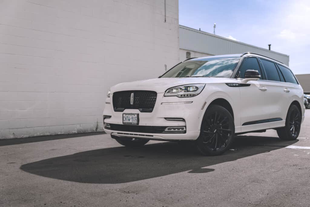 White luxury SUV parked on pavement with black wheels, showcasing a sleek design and modern features, against a neutral building backdrop.