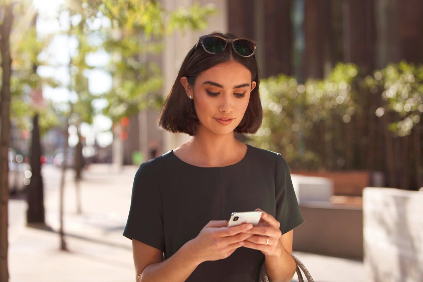 Woman using smartphone app to control car features, with vehicles blurred in the background.
