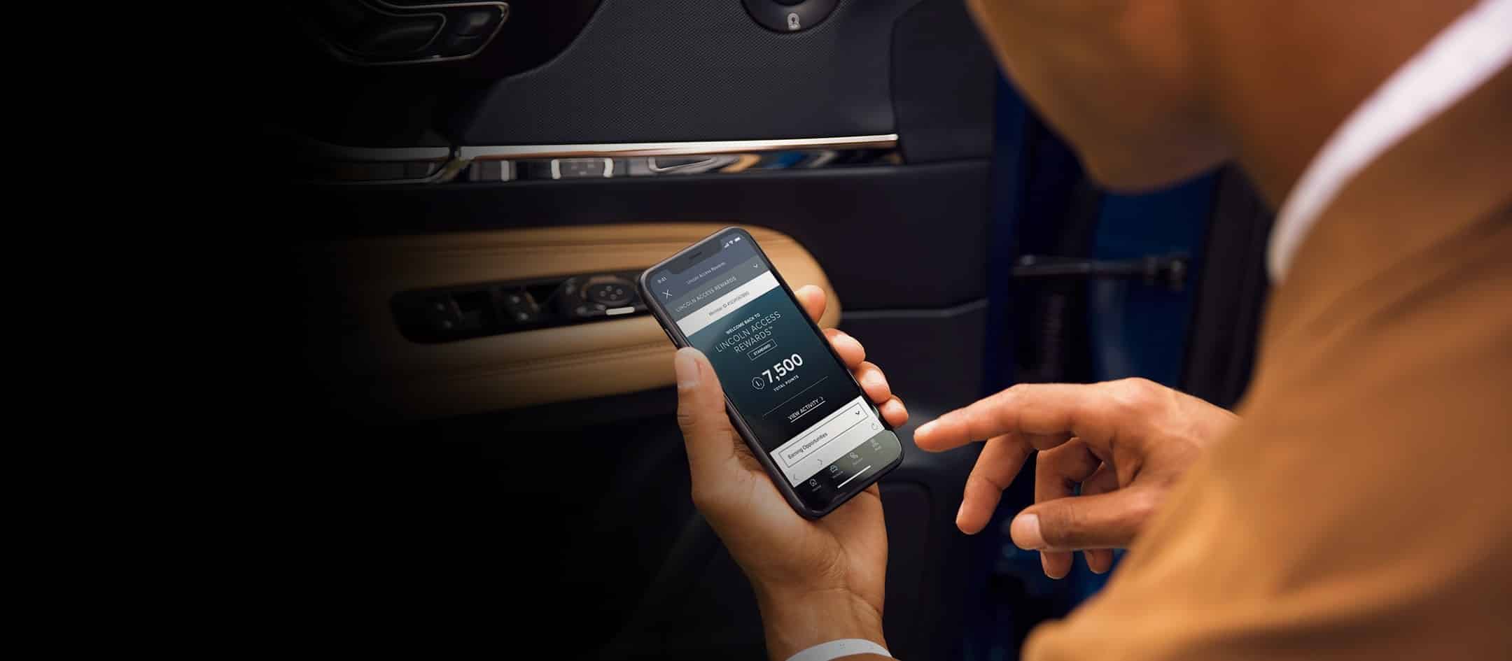 Person using a smartphone with Lincoln Access Rewards app inside a car, displaying 7,500 points.