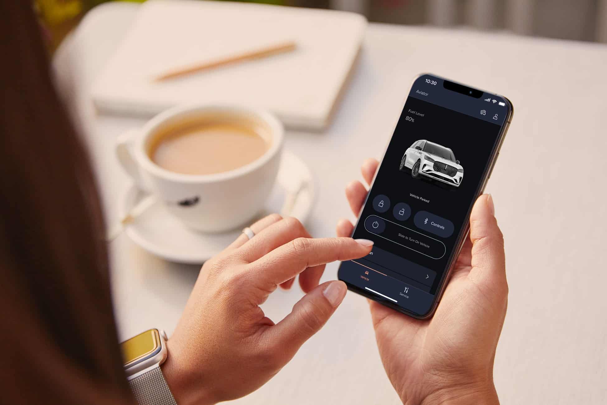 Person using smartphone app to control car features; coffee cup nearby.