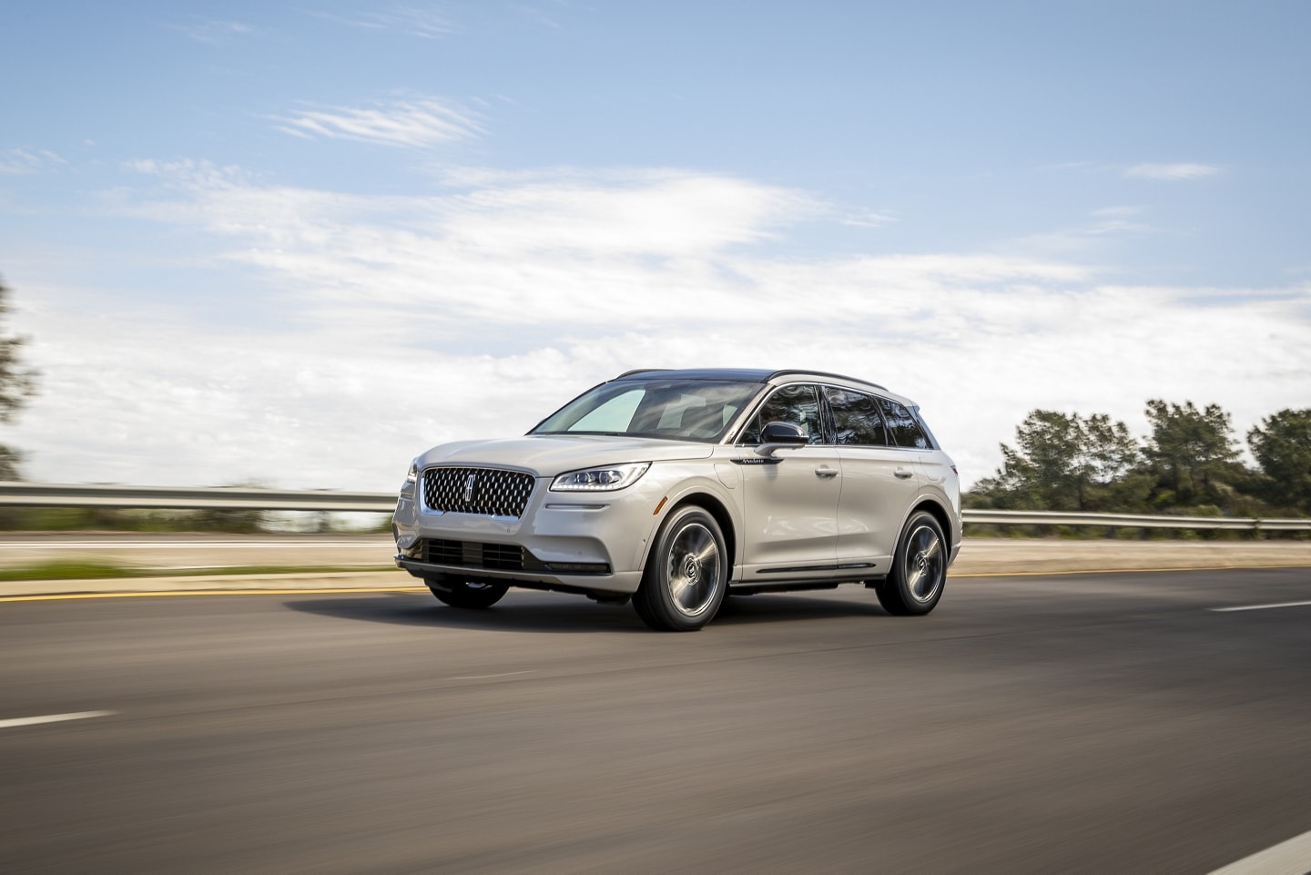 A sleek silver SUV driving along a scenic highway, showcasing modern design and performance. The vehicle is a Lincoln Corsair, highlighting its elegant exterior and spacious structure against a backdrop of trees and a clear sky.