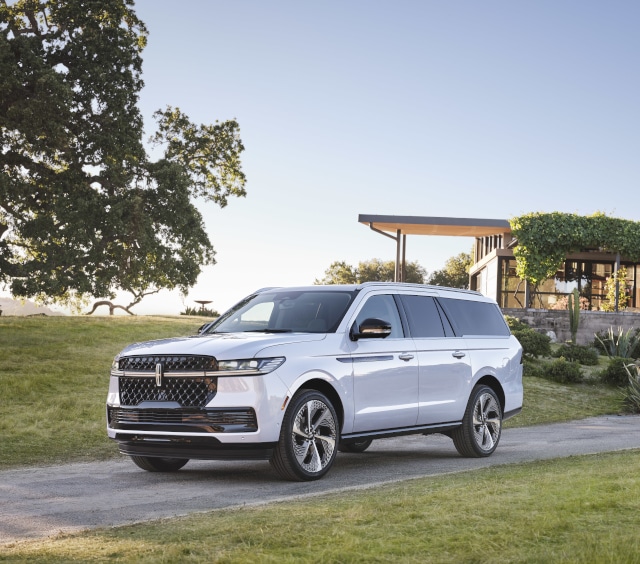 Luxury SUV parked on a scenic driveway with modern architecture in the background, showcasing its sleek white exterior and distinctive grille design.