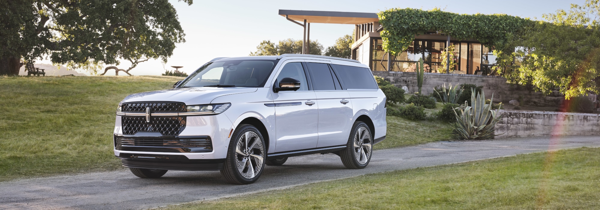 A sleek and modern luxury SUV parked on a scenic driveway, surrounded by lush greenery and a contemporary house in the background, showcasing its stylish design and spacious build.