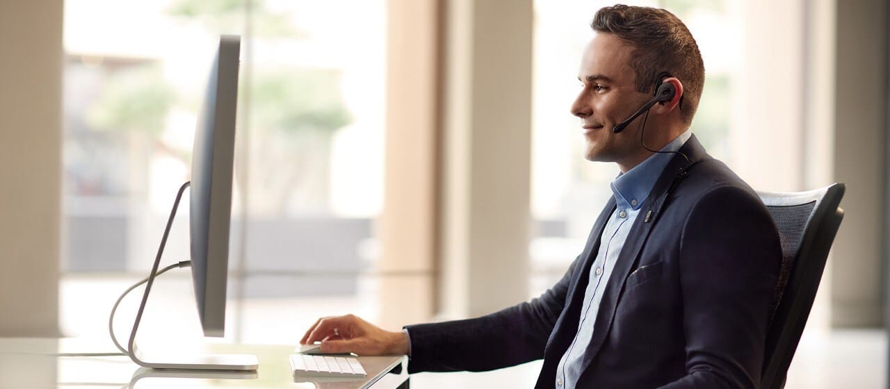 Professional man wearing a headset working at a computer desk, focusing on the screen in a modern office environment.