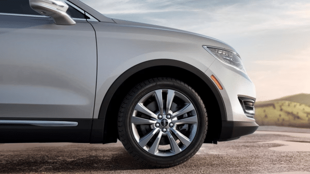 Silver SUV front wheel and fender, showcasing sleek design and luxurious style against a scenic backdrop.