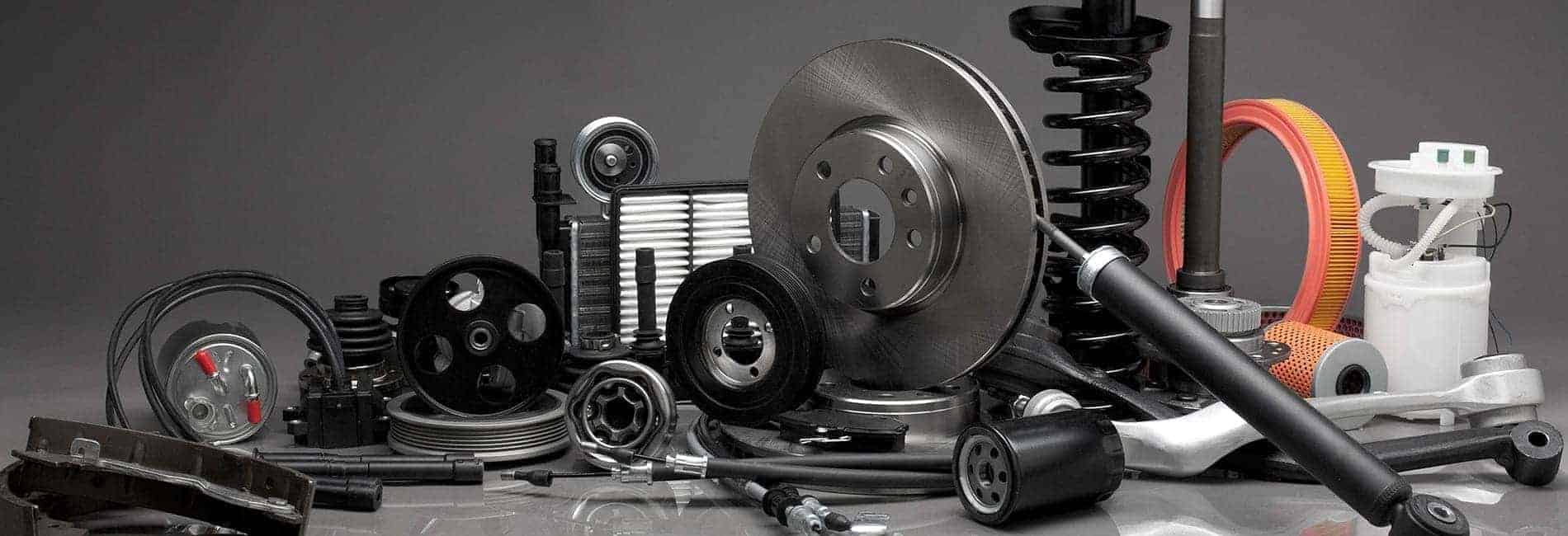 Assorted car parts including brake discs, filters, and shock absorbers on a gray background.